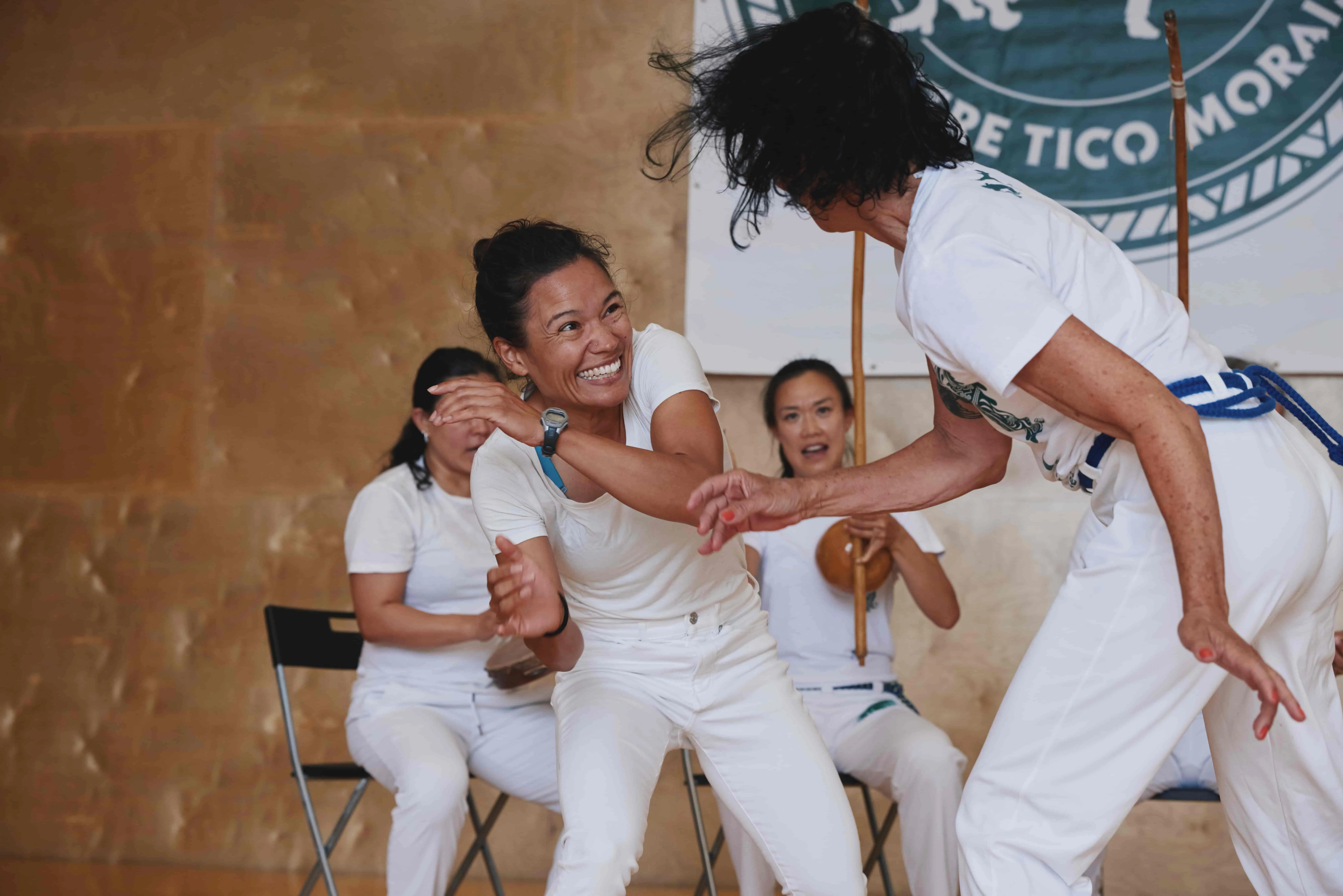 Two students play capoeira in a training roda, while others play instruments.